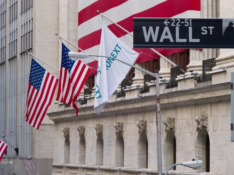 The Wall Street sign outside the New York Stock Exchange, with United States flags flying above the building.