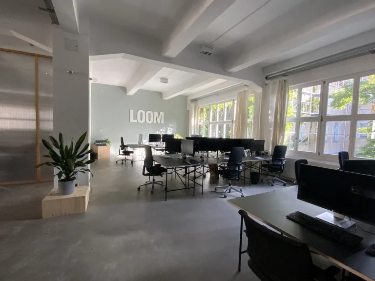 A modern office floor with rows of empty desks, monitors and chairs and no staff present.